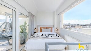 A modern bedroom with a large bed, a view of the city, and a balcony with a chair. - 3-Storey Family Home, City View & Private Parking! (Athina)