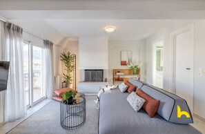 A modern living room with a grey sofa, a small round coffee table, and a fireplace. There is a TV on the left and a plant on the right. - 3-Storey Family Home, City View & Private Parking! (Athina)