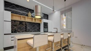 Eine moderne Küche mit Marmor-Spritzschutz, Holzregalen und einer zentralen Kochinsel mit Barhocker.