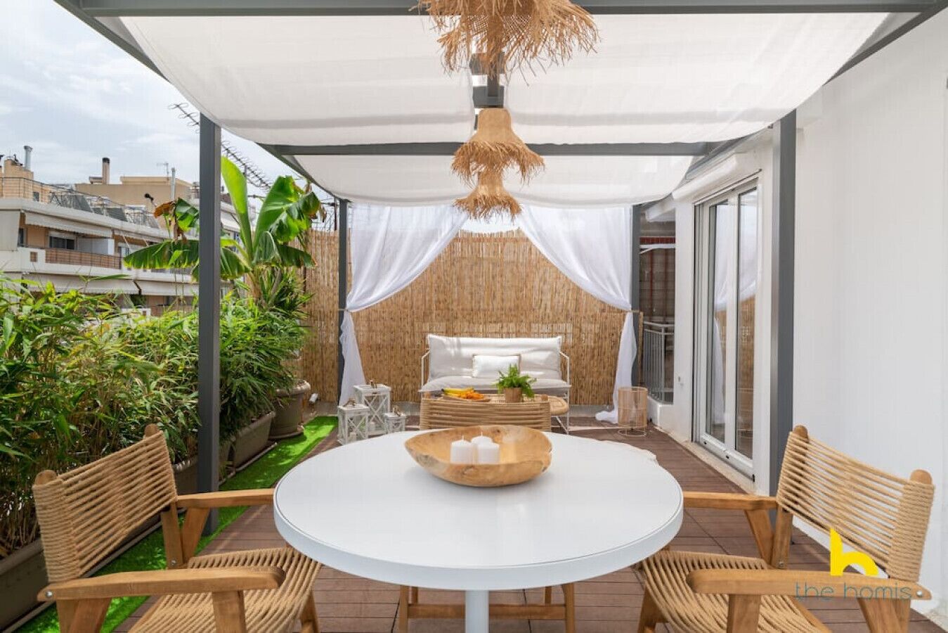 A patio with a round table and wicker chairs, a white sofa, and a hanging light fixture.