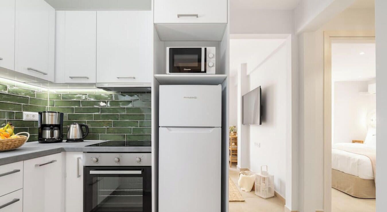 A modern kitchen with white cabinets, a built-in oven, a microwave, and a coffee maker.