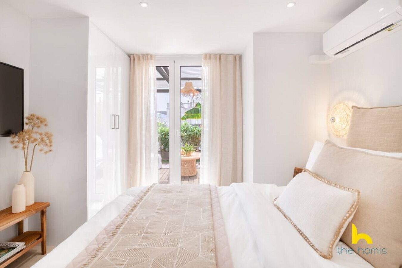 A modern bedroom with a large bed, a bedside table, a TV, and a view of the outdoors through a glass door.