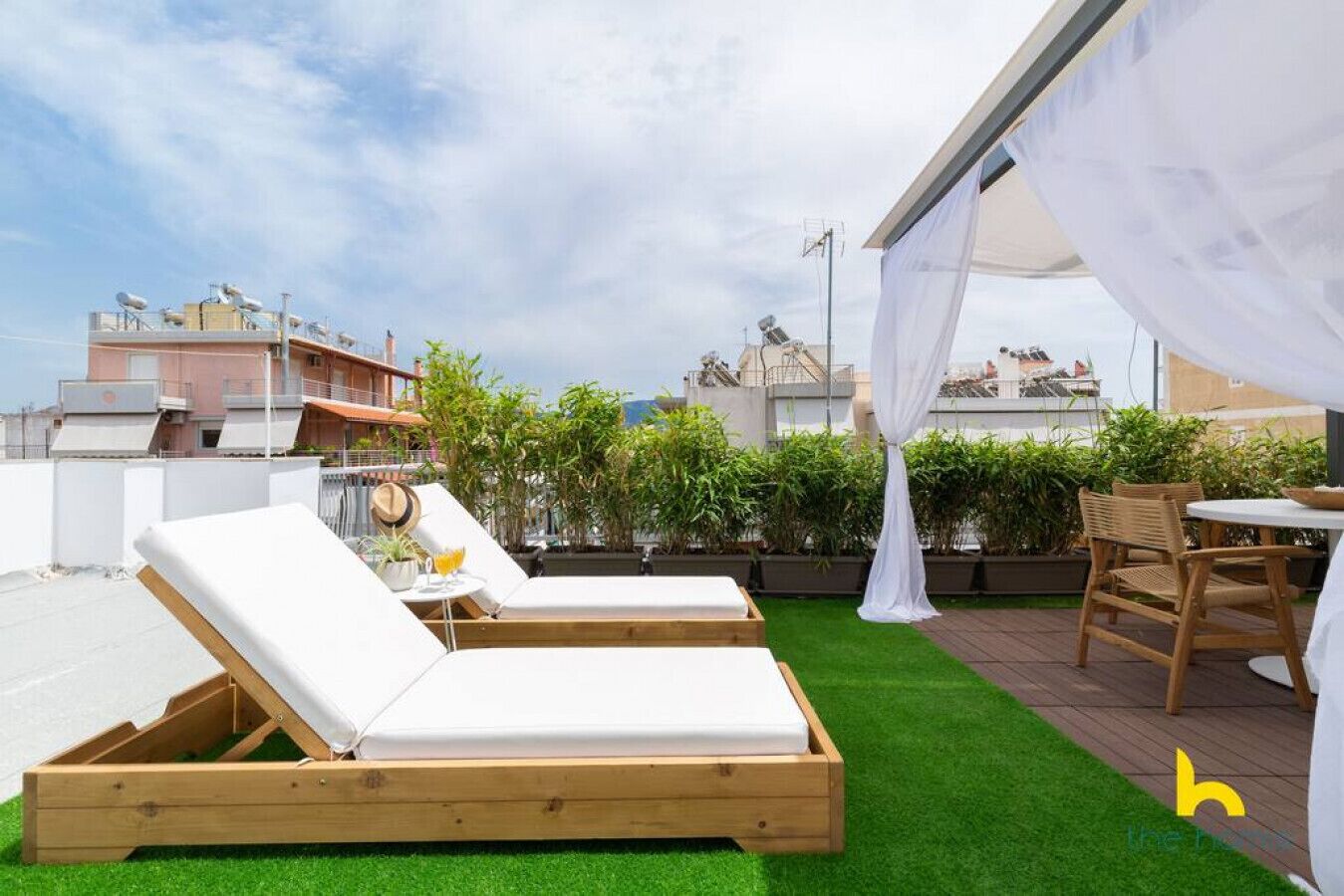 A rooftop terrace with two wooden lounge chairs, a small table with a drink, and a white canopy.
