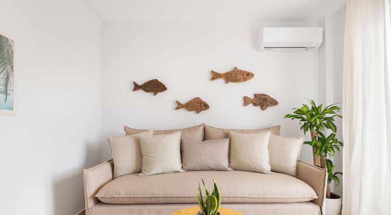 Un salon avec un canapé beige, quatre décorations murales représentant des poissons, une plante en pot et un climatiseur blanc.