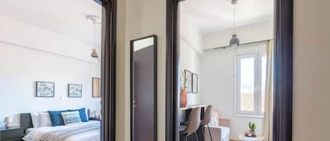 A bedroom with a bed, bedside table, and a desk with a chair. There is a window with curtains and a view of the outside.