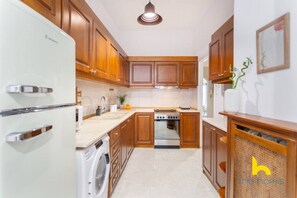 A compact kitchen with wooden cabinets, a built-in oven, a washing machine, and a sink. - Grand Family APT with Courtyard near Acropolis! (Athina)