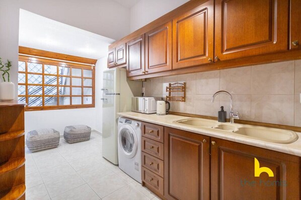 A compact kitchen with wooden cabinets, a washing machine, and a sink. - Grand Family APT with Courtyard near Acropolis! (Athina)