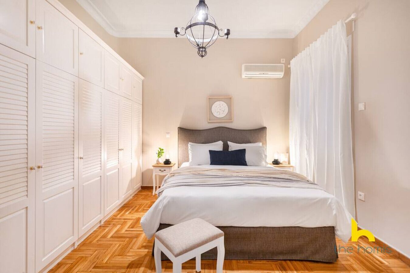 A bedroom with a bed, a nightstand, a chair, a wardrobe, and a chandelier.