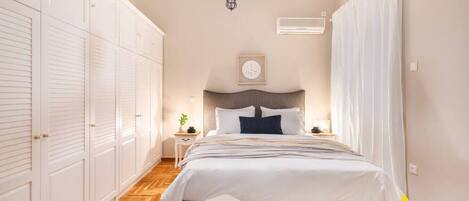A bedroom with a bed, a nightstand, a chair, a wardrobe, and a chandelier.