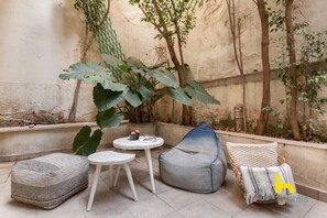 A small patio area with a round table, a bean bag, and a cushioned bench. - Grand Family APT with Courtyard near Acropolis! (Athina)