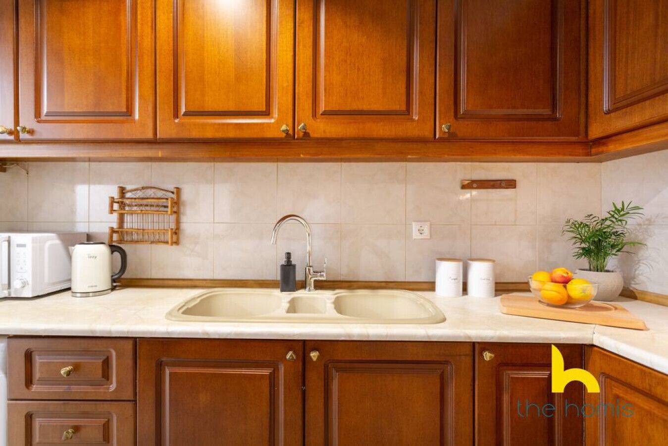 A kitchen with wooden cabinets, a double sink, a toaster, a kettle, and a bowl of fruit on the counter.