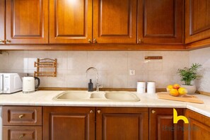 A kitchen with wooden cabinets, a double sink, a toaster, a kettle, and a bowl of fruit on the counter. - Grand Family APT with Courtyard near Acropolis! (Athina)