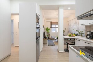 A modern kitchen with built-in appliances, a dining area with a table and chairs, and a living space with a sofa and a plant. - The Urban Jungle Escape Corner APT Near Acropolis (Athina)
