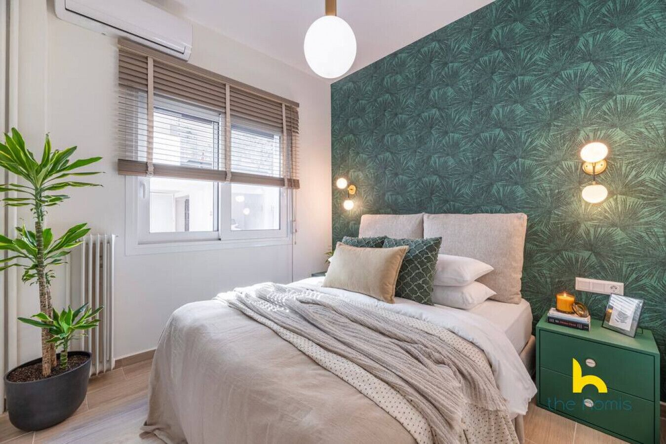 A bedroom with a bed, a potted plant, a radiator, and a green nightstand with a logo.