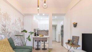 A modern living room with a green sofa, a TV, and a dining area with two bar stools. - The Urban Jungle Escape Corner APT Near Acropolis (Athina)