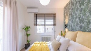 A bedroom with a bed, a window with blinds, a radiator, a potted plant, and a wall with a leaf pattern. - The Urban Jungle Escape Corner APT Near Acropolis (Athina)