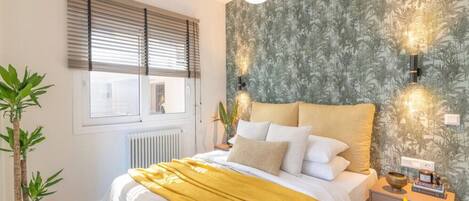 A bedroom with a bed, bedside tables, a potted plant, and a window with blinds.