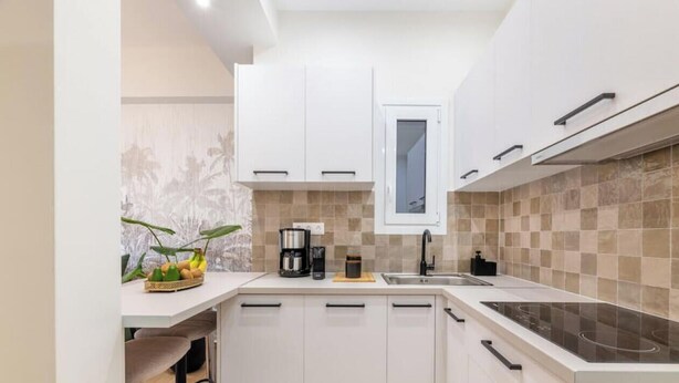 A modern kitchen with white cabinets, a black stove, and a tiled backsplash. - The Urban Jungle Escape Corner APT Near Acropolis (Athina)