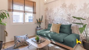 A modern living room with a green sofa, a coffee table with a plant, and a window with blinds. - The Urban Jungle Escape Corner APT Near Acropolis (Athina)