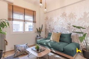 A modern living room with a green sofa, a coffee table with a plant, and a window with blinds. - The Urban Jungle Escape Corner APT Near Acropolis (Athina)