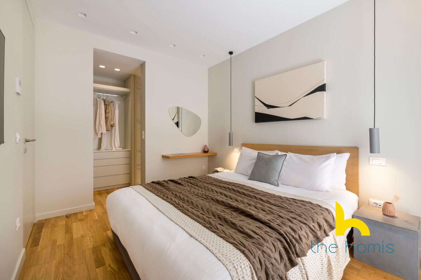 A modern bedroom with a large bed, a bedside table, a mirror, and a wall-mounted abstract art piece.