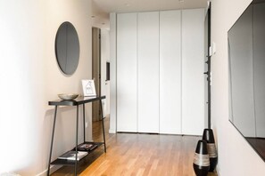 A modern interior with a wooden floor, a black metal side table with a bowl and a framed sign, and a white closet with sliding doors. - Urban APT with Stunning Acropolis View & Roofdeck (Athina)