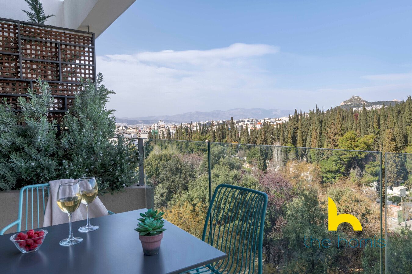 Un balcon avec une table, deux verres à vin, un bol de framboises et une plante en pot.