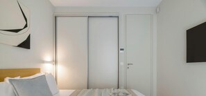 A hotel room with a bed, a bedside table, a wall-mounted TV, and a wardrobe. - Urban APT with Stunning Acropolis View & Roofdeck (Athina)