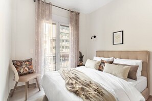 Ein Schlafzimmer mit Bett, Sessel und Balkon mit Vorhängen.