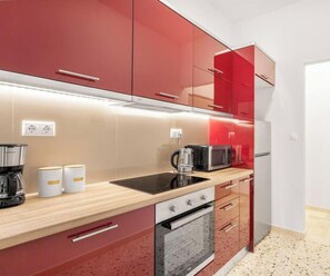 A modern kitchen with red cabinets, a black induction cooktop, a microwave, and a built-in oven. - Quiet, Minimalist Base w/ Balcony near Metro (Athina)
