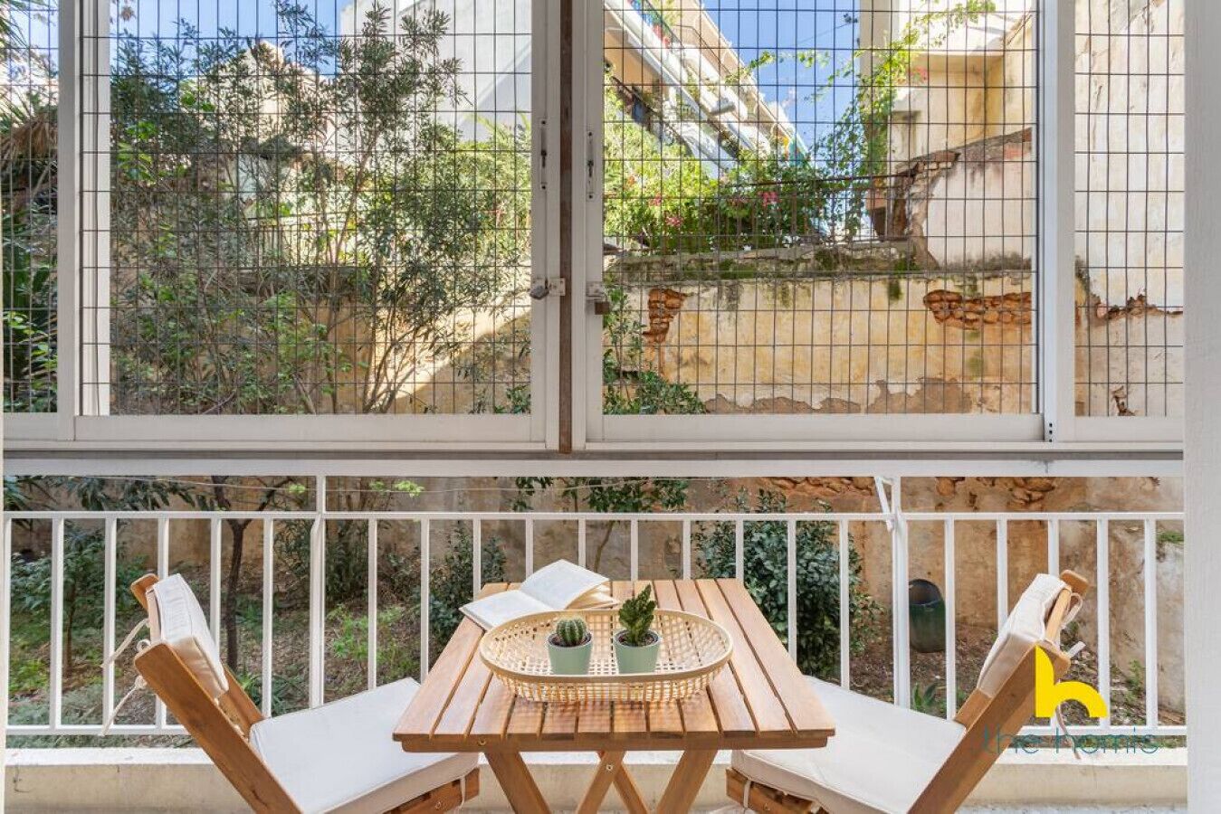 Ein Balkon mit Holztisch, zwei Stühlen und einem kleinen Topfpflanzen.
