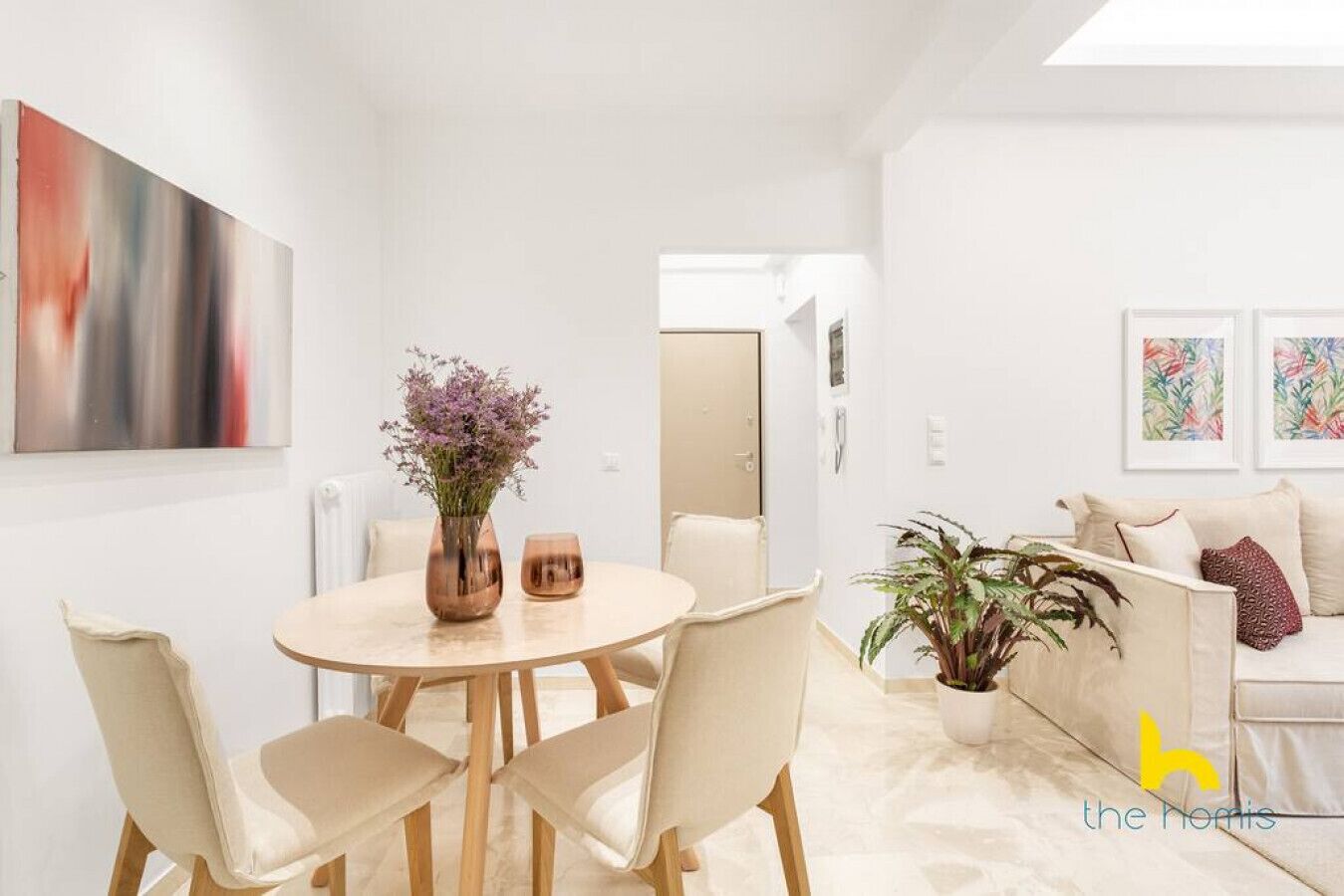 A modern living room with a round table, beige chairs, a sofa, and a potted plant.