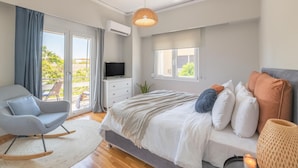 Un dormitorio moderno con cama, televisor, sillón y vistas al balcón.