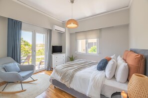 Ein modernes Schlafzimmer mit Bett, Fernseher, Sessel und Balkonblick.