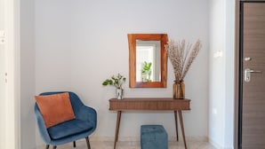 Un interior moderno con un sillón azul, un taburete pequeño, una consola de madera, un espejo y un jarrón con plantas secas.