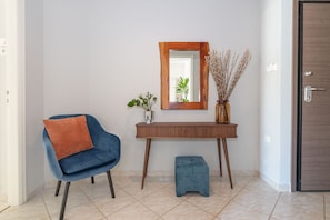 Ein modernes Interieur mit einem blauen Sessel, einem kleinen Hocker, einem Holztischchen, einem Spiegel und einer Vase mit getrockneten Pflanzen.