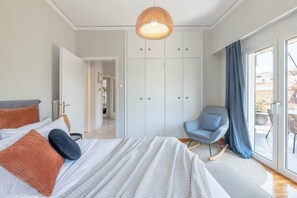 Ein Schlafzimmer mit Bett, einem Sessel, einem Kleiderschrank und Blick durch eine Glastür.