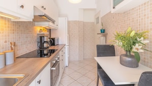 Cocina compacta con estufa, cafetera y comedor con mesa y sillas.
