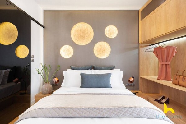 Quarto moderno com cama grande, mesas de cabeceira, guarda-roupa e luminária suspensa.