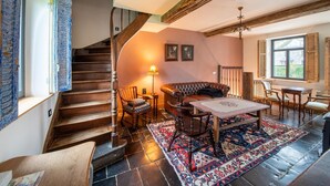 A cozy living room with a wooden staircase, a leather sofa, a patterned rug, and a table with chairs. - Charming holiday home with garden (Dinant)