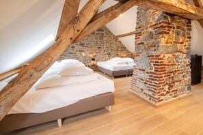 Ein Schlafzimmer mit schrägverdeckter Decke, freiliegenden Holzbalken und einer Steinwand. Es gibt zwei Betten mit weißer Bettwäsche.
