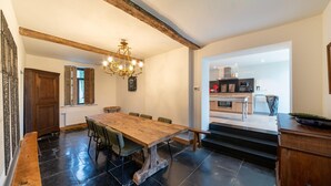 A spacious dining area with a large wooden table and chairs, a chandelier, and a view into a modern kitchen. - Charming holiday home with garden (Dinant)