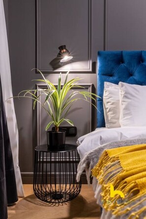 A bedroom with a blue headboard, a bedside table with a potted plant, and a lamp. - Unique Urban Cave w/ Pool Table Near Acropolis! (Athina)