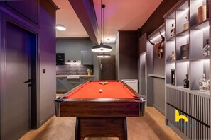 A modern pool table in a well-lit room with a kitchen in the background and a liquor cabinet on the right. - Unique Urban Cave w/ Pool Table Near Acropolis! (Athina)