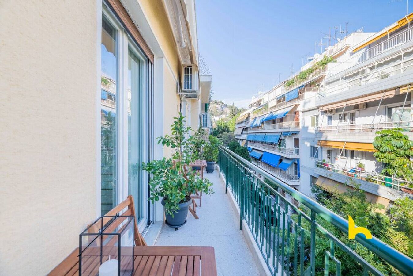 A balcony with a wooden bench, potted plants, and a view of a narrow street with buildings and boats.