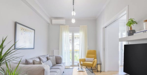 A modern living room with a sofa, a yellow armchair, a TV, and a plant. - Sun-Splashed 2-BDR Corner APT with Hillside views! (Athina)
