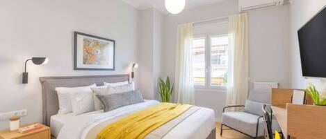 Una habitación de hotel moderna con cama, mesita de noche, lámpara, obra de arte, ventana, silla y televisión.