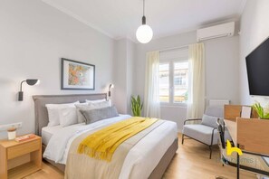 Une chambre d’hôtel moderne équipée d’un lit, d’une table de chevet, d’une lampe, d’œuvres d’art, d’une fenêtre, d’une chaise et d’un téléviseur.