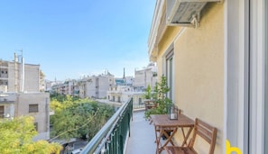 Un balcon avec une table et des chaises, donnant sur un paysage urbain avec des bâtiments et de la verdure.