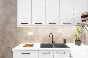 A kitchen with white cabinets, a black sink, and a hexagonal tile backsplash.